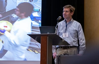 A male speaker presenting at a podium at the Lab Design Conference
