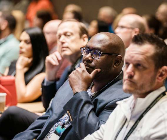 A crowd of attendees sit in the audience of a Lending Tech Live session